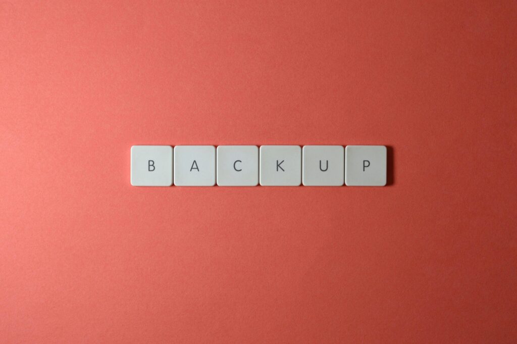 Close-up of keyboard keys spelling 'BACKUP' placed on a coral-colored surface.